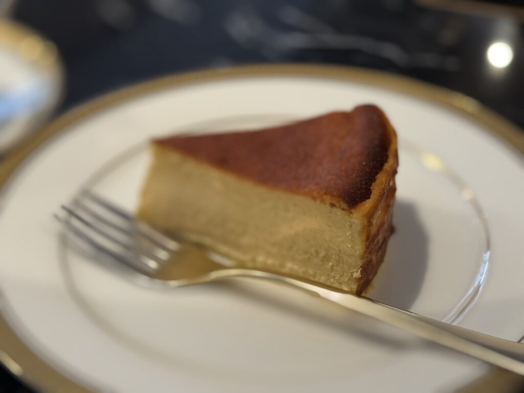 金縁の白い皿に乗ったバスクチーズケーキとフォークのクローズアップ