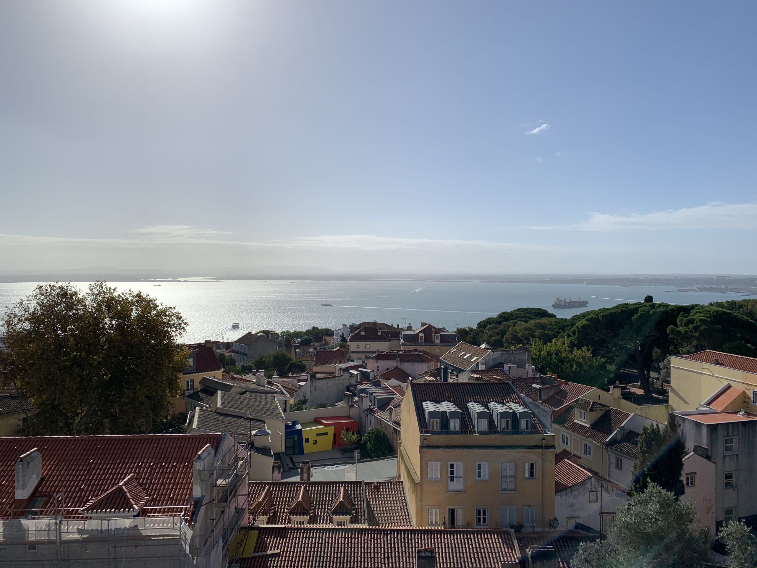 Red-tiled rooftops overlooking the shimmering Tagus River with strong sun glare