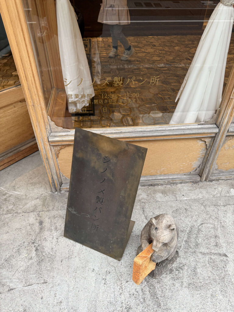 「シノノメ製パン所」の真鍮看板と、パンをかじる木彫りの熊の置物