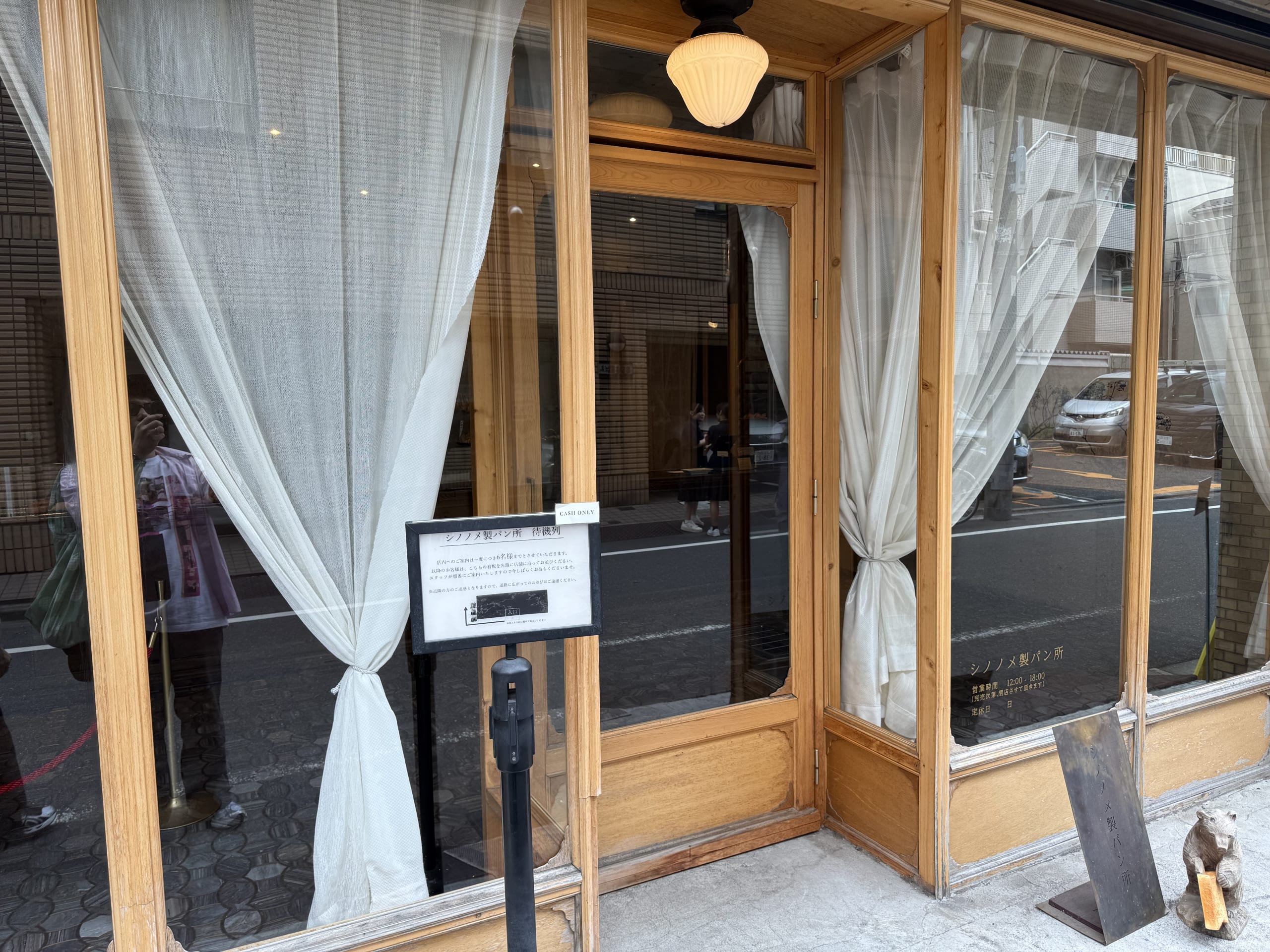 Exterior of Shinonome Bakery featuring wooden framing, white curtains, and an entrance guideline sign