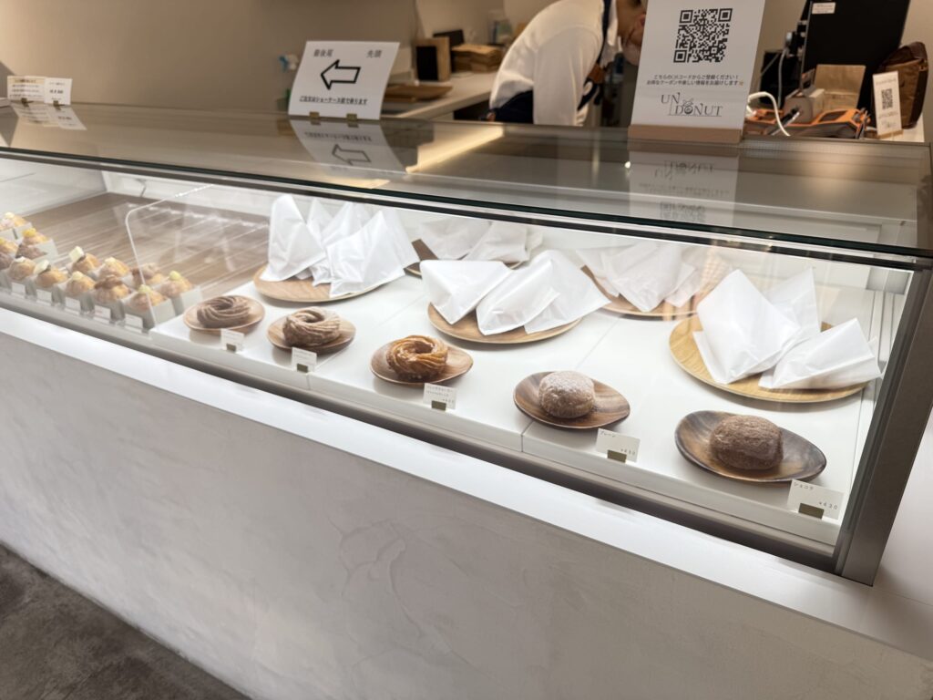 Display case featuring French crullers, plain, and chocolate donuts on wooden plates