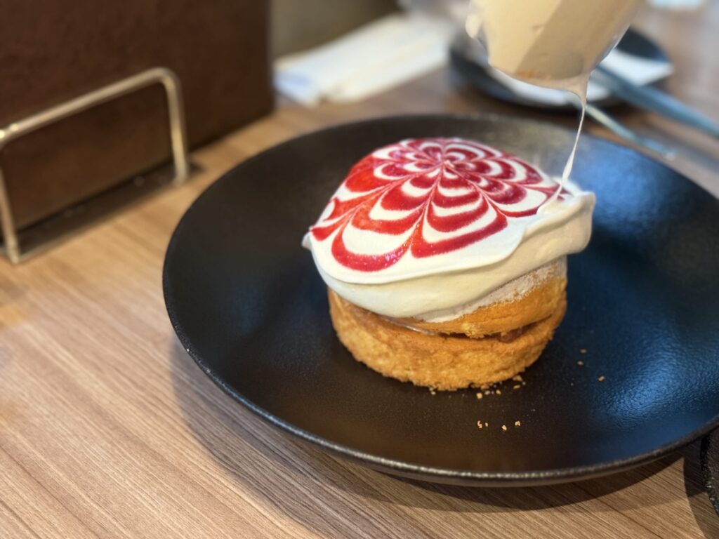 A thick pancake on a black plate covered in white cream with a red floral swirl pattern resembling a blooming flower