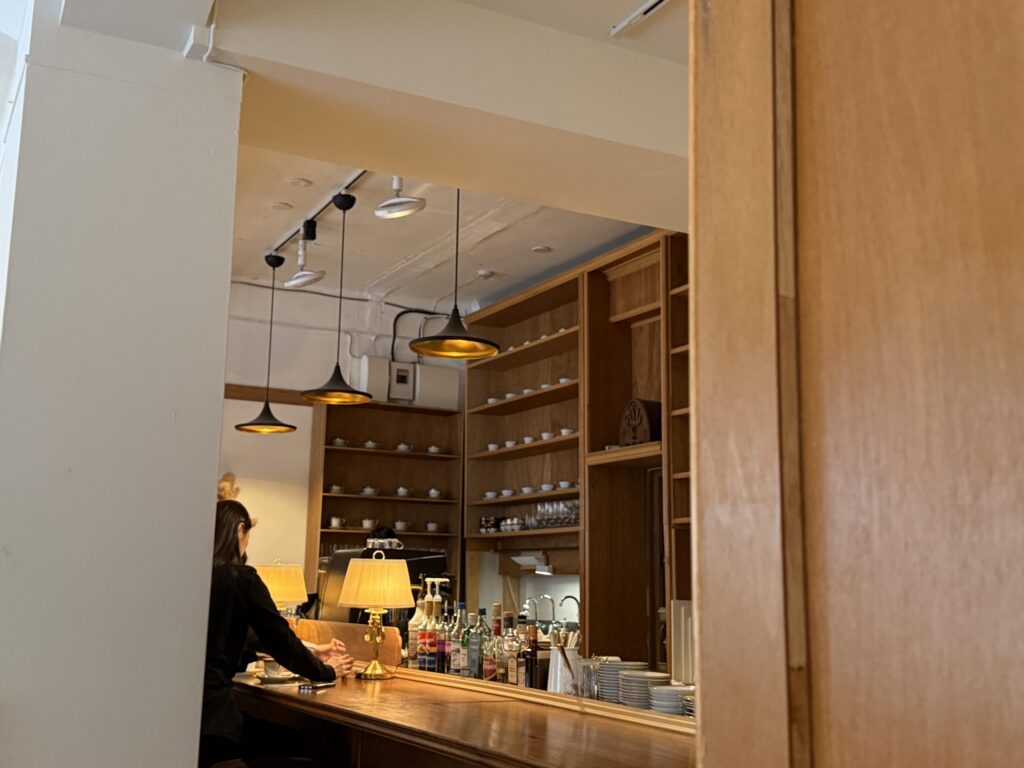 View of a cafe counter with wooden shelves filled with white cups and warm pendant lighting