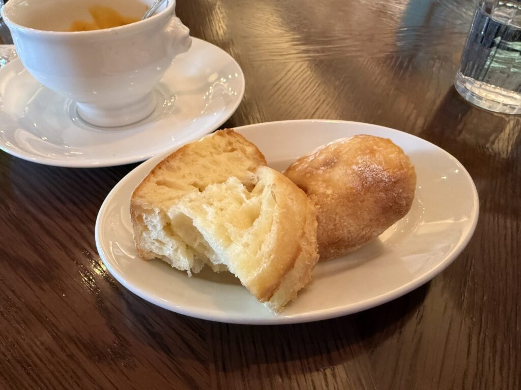 Two pieces of fluffy bread on a white oval plate with a cup of orange soup in the background