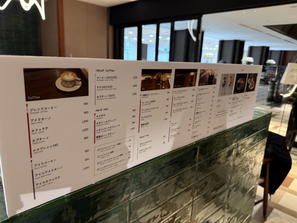 緑色のタイルカウンターに置かれたドリンクメニューボード。コーヒー、デカフェ、紅茶などの種類と価格が記載されている。