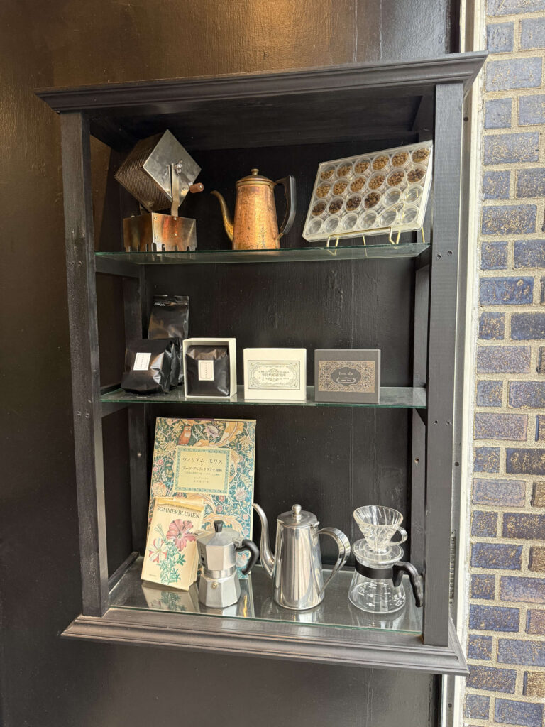 Black shelf displaying coffee beans, copper kettle, William Morris book, and brewing equipment