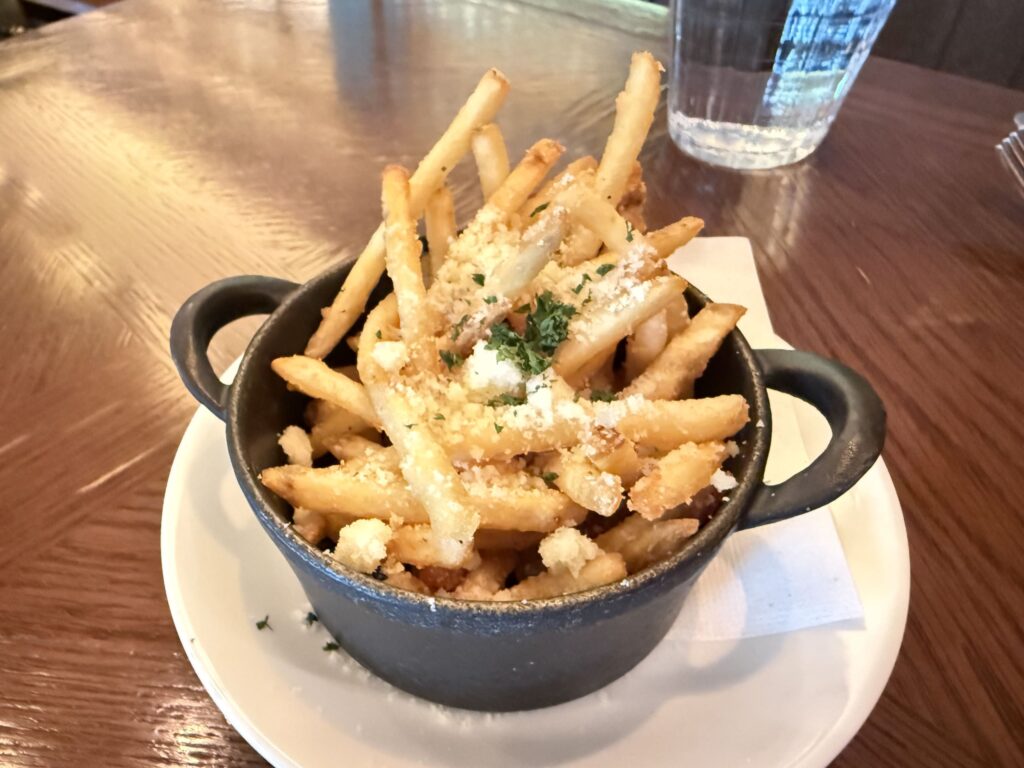 French fries topped with grated parmesan cheese and parsley served in a small black two-handled dish