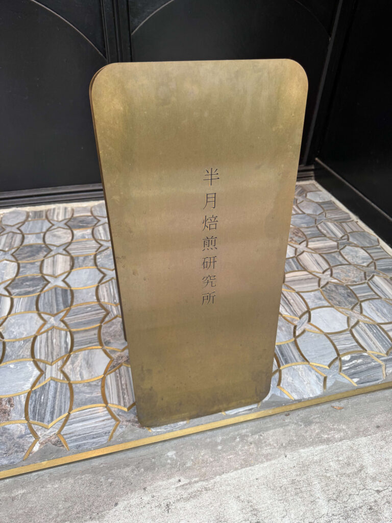 A heavy brass standing sign engraved with the text 'Hangetsu Baisen Kenkyujo' on a tiled floor