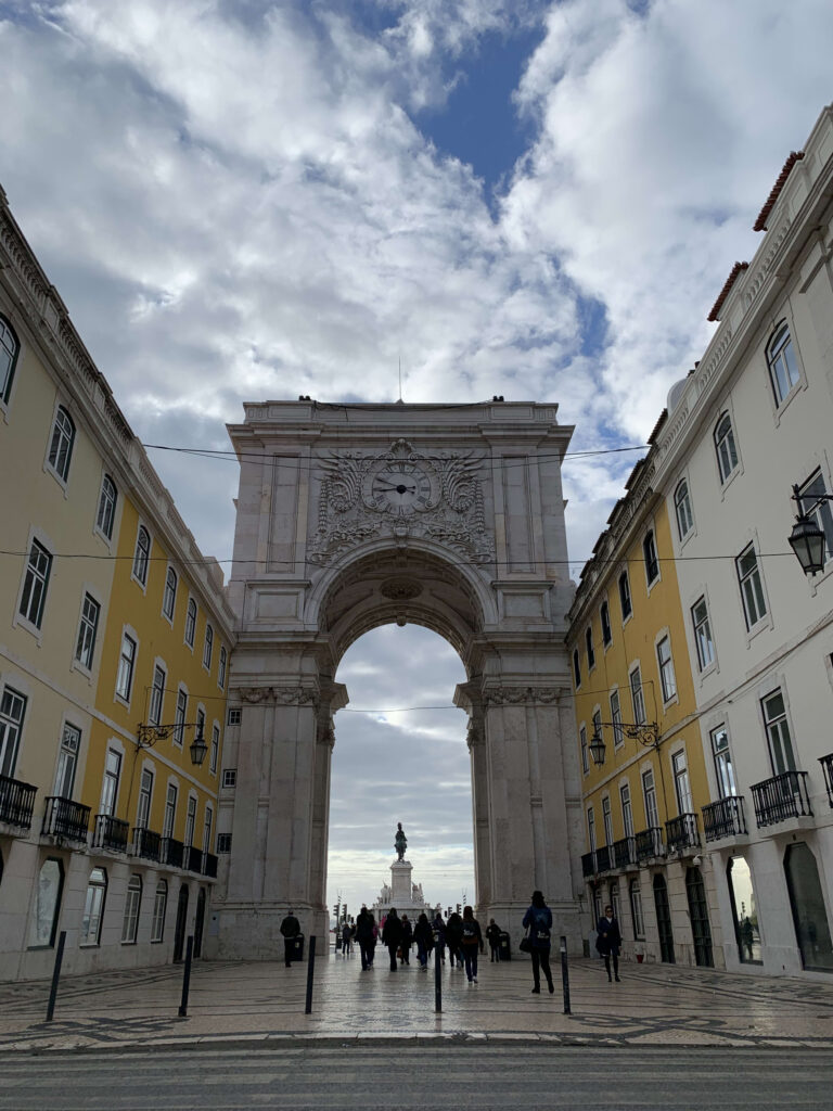 Low-angle view of the Rua Augusta Arch in Lisbon, framing the equestrian statue of King José I through its central opening against a cloudy sky