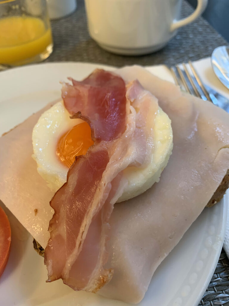 Open-faced breakfast sandwich featuring ham, a soft sunny-side-up egg, and bacon on toast