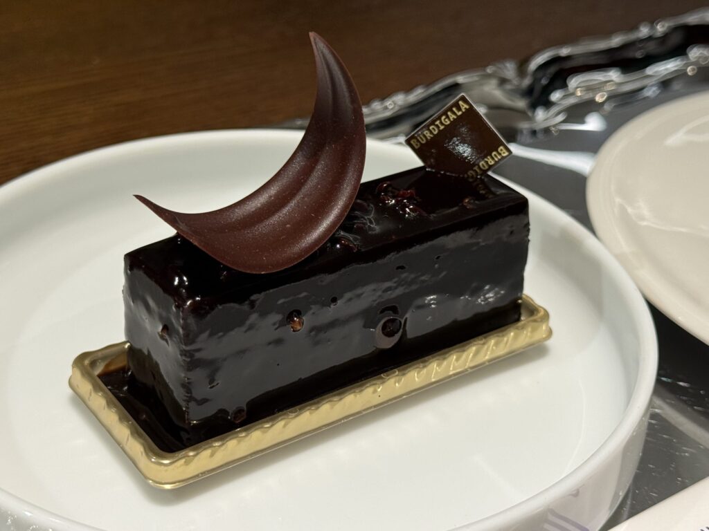 Close-up of a glossy rectangular chocolate cake called Miroir Chocolat topped with a crescent-shaped chocolate garnish