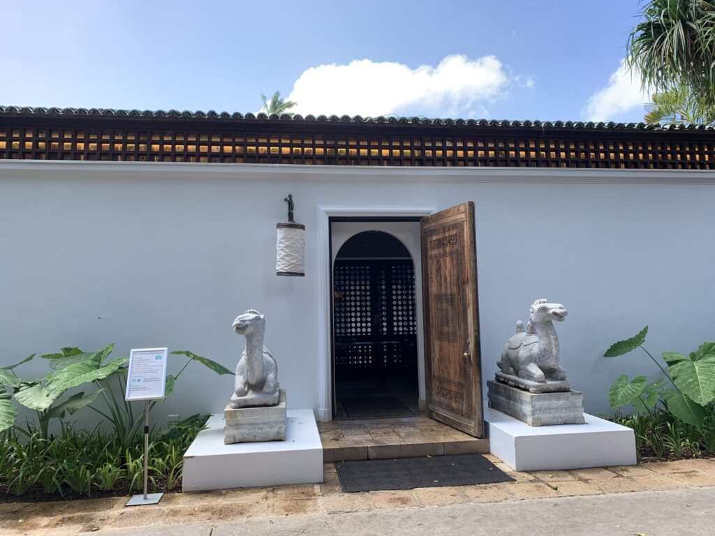 白い壁の建物の入り口。彫刻が施された木製の扉と、その両脇に鎮座する2体のラクダの石像。