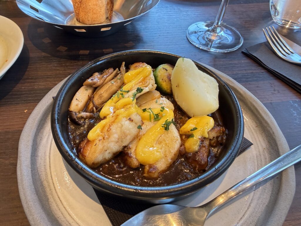 Sète-style cod served in a black dish with yellow sauce, boiled potato, and mushrooms