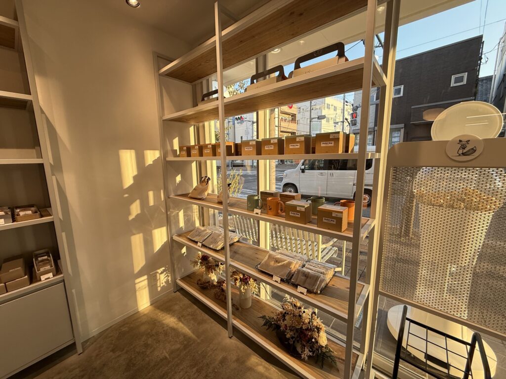 Shop display shelves by the window featuring mugs and tote bags illuminated by warm evening sunlight