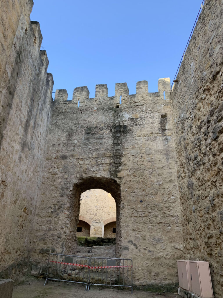 青空を背景にした古城の高い石壁とアーチ状の門、手前には安全柵がある