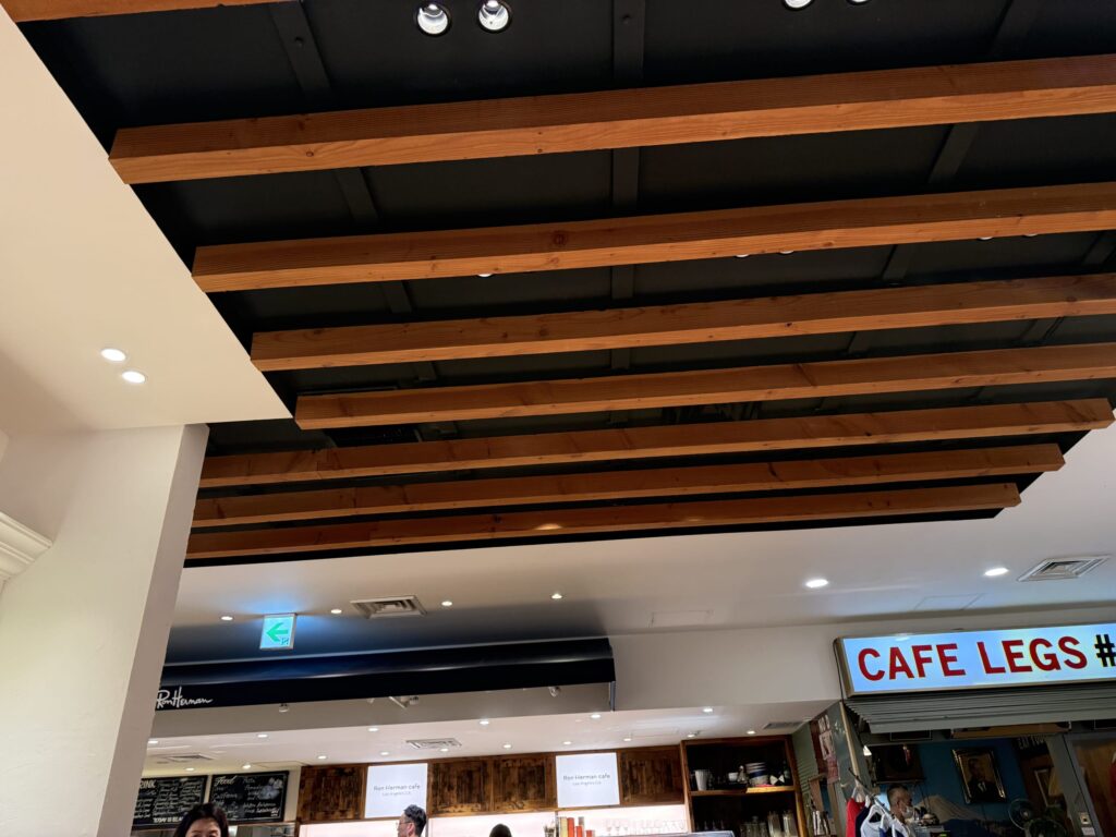 黒い天井に木製の梁が並ぶスタイリッシュなカフェ店内の天井とCAFE LEGSの看板
