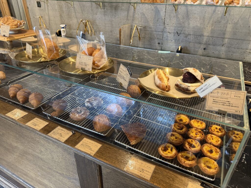 パン屋のショーケースに並ぶあんバターフランス、エッグタルト、クロワッサンなどの焼き菓子