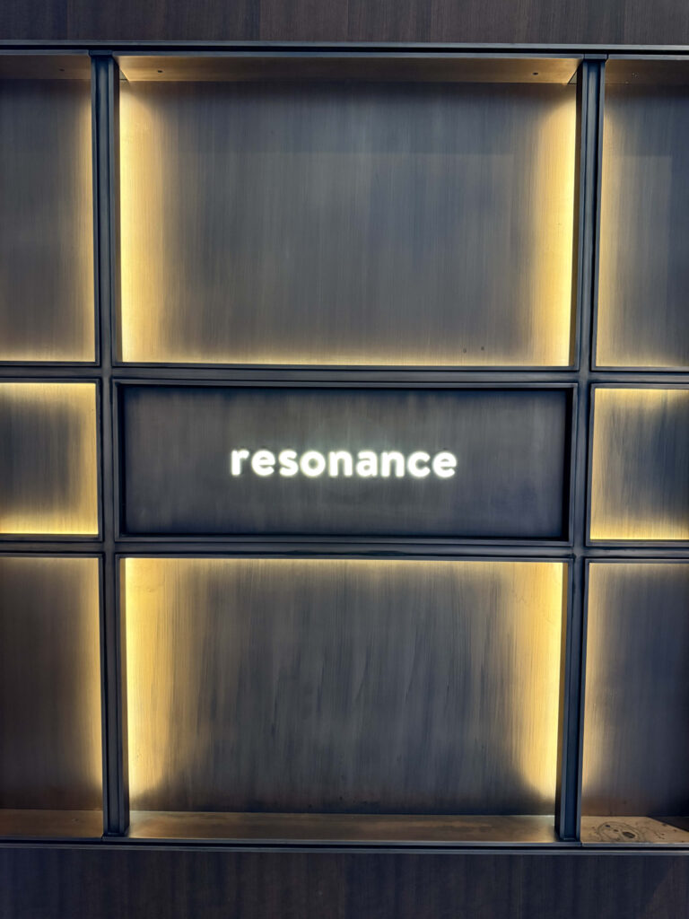 ダークグレーのパネル背景に温かなバックライトが灯り、中央に「resonance」の文字が白く発光している壁面看板
