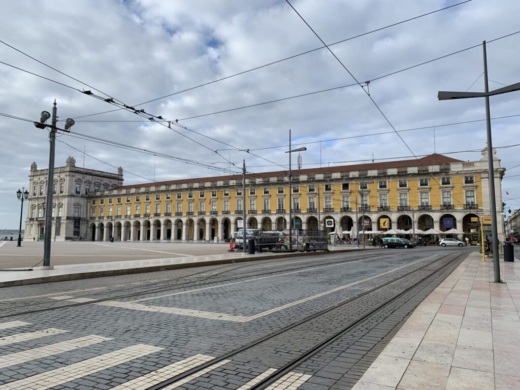 石畳の広場とトラムの線路、奥に広がる黄色い回廊付きの庁舎