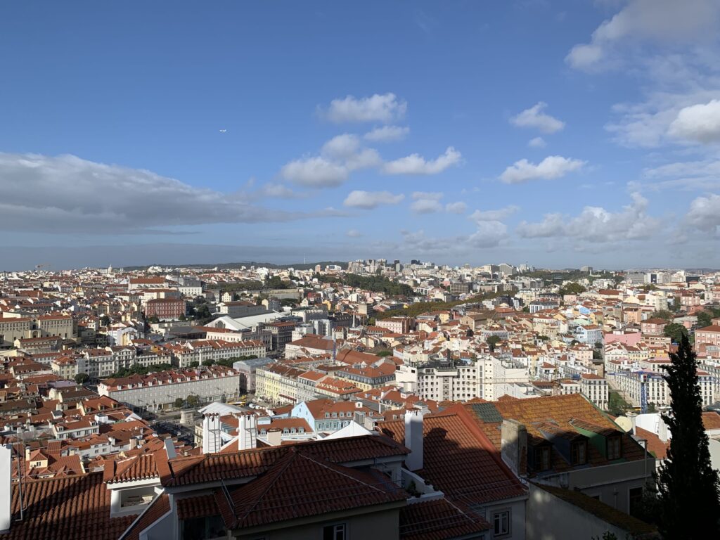 青空と白い雲の下に広がるリスボンの赤い屋根の街並みの広角写真