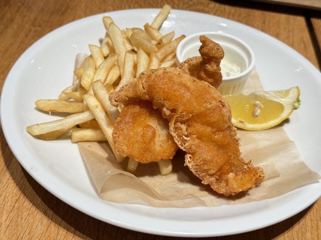 Golden brown fish and chips served on a white plate with french fries, tartar sauce, and a lemon wedge