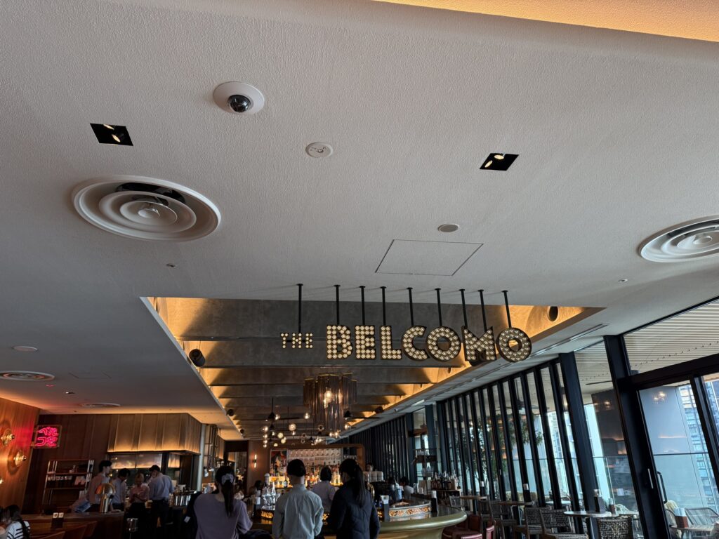 Interior of THE BELCOMO restaurant featuring a large illuminated marquee sign hanging from the ceiling
