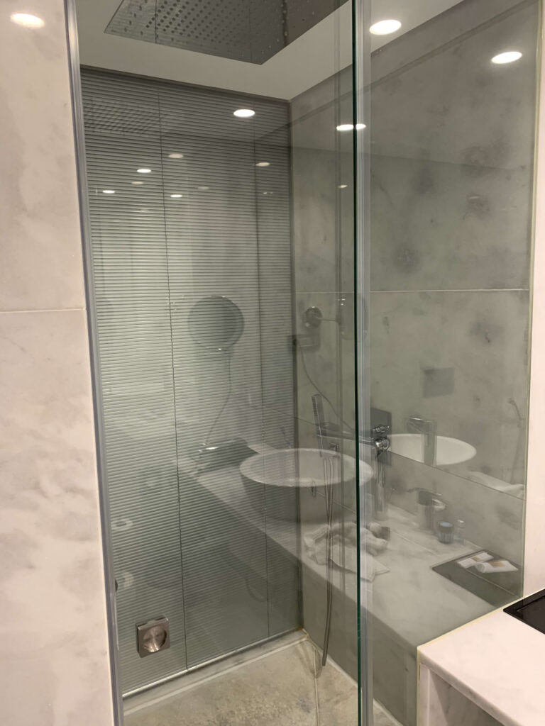 Glass-enclosed shower booth featuring a ceiling-mounted rain shower and blind-style wall design