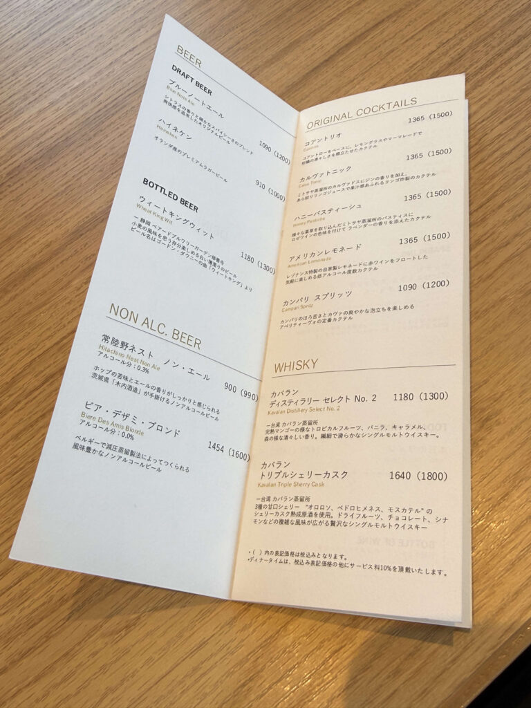 木目のテーブルに置かれたビール、カクテル、ウイスキーが記載されたドリンクメニュー表