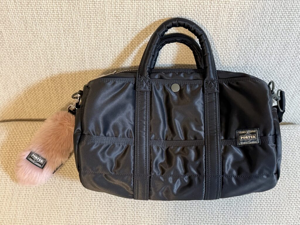 Black Porter Boston bag with a pink fur charm in hand-held style sitting on a textured surface