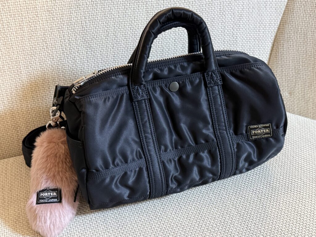 椅子の上に置かれたPORTERの黒いボストンバッグSとピンクのファーチャーム