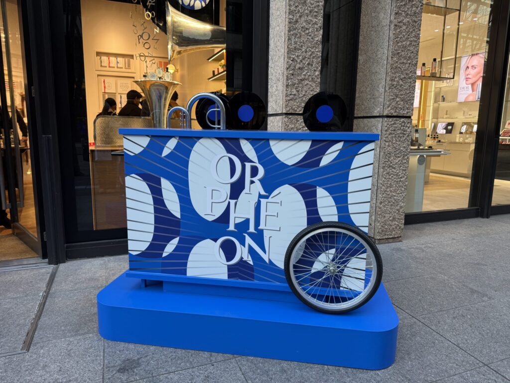 Blue display unit themed around 'Orphéon' featuring a bicycle wheel and graphic text outside a store