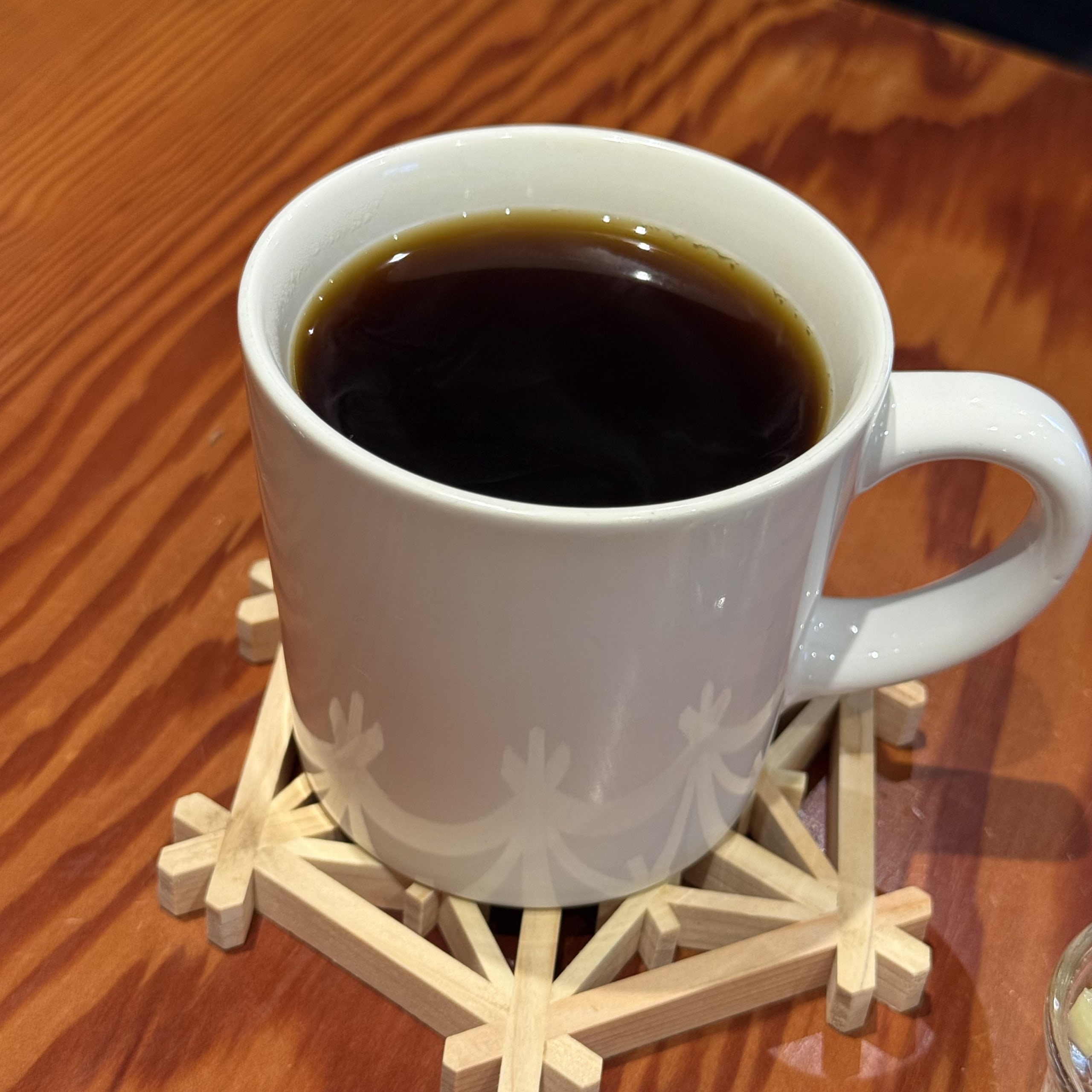 木目テーブルに置かれた木製コースターと白いマグカップのコーヒー。