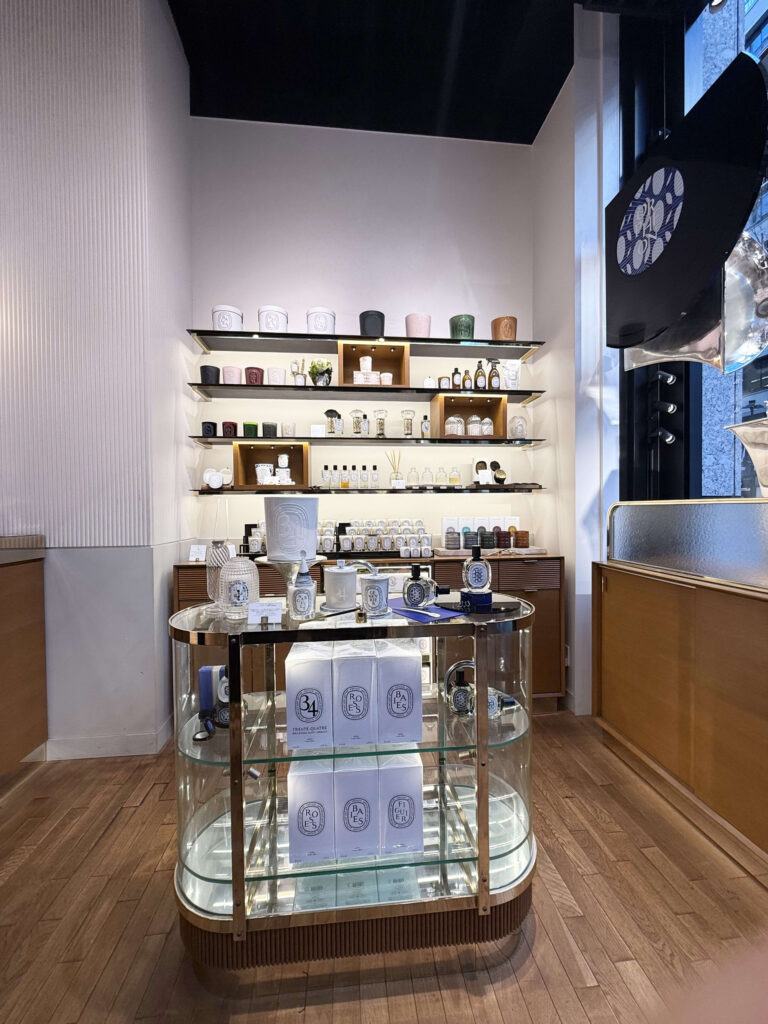 Interior of Diptyque store featuring wall-mounted shelves filled with candles and a central circular glass display unit with boxed products