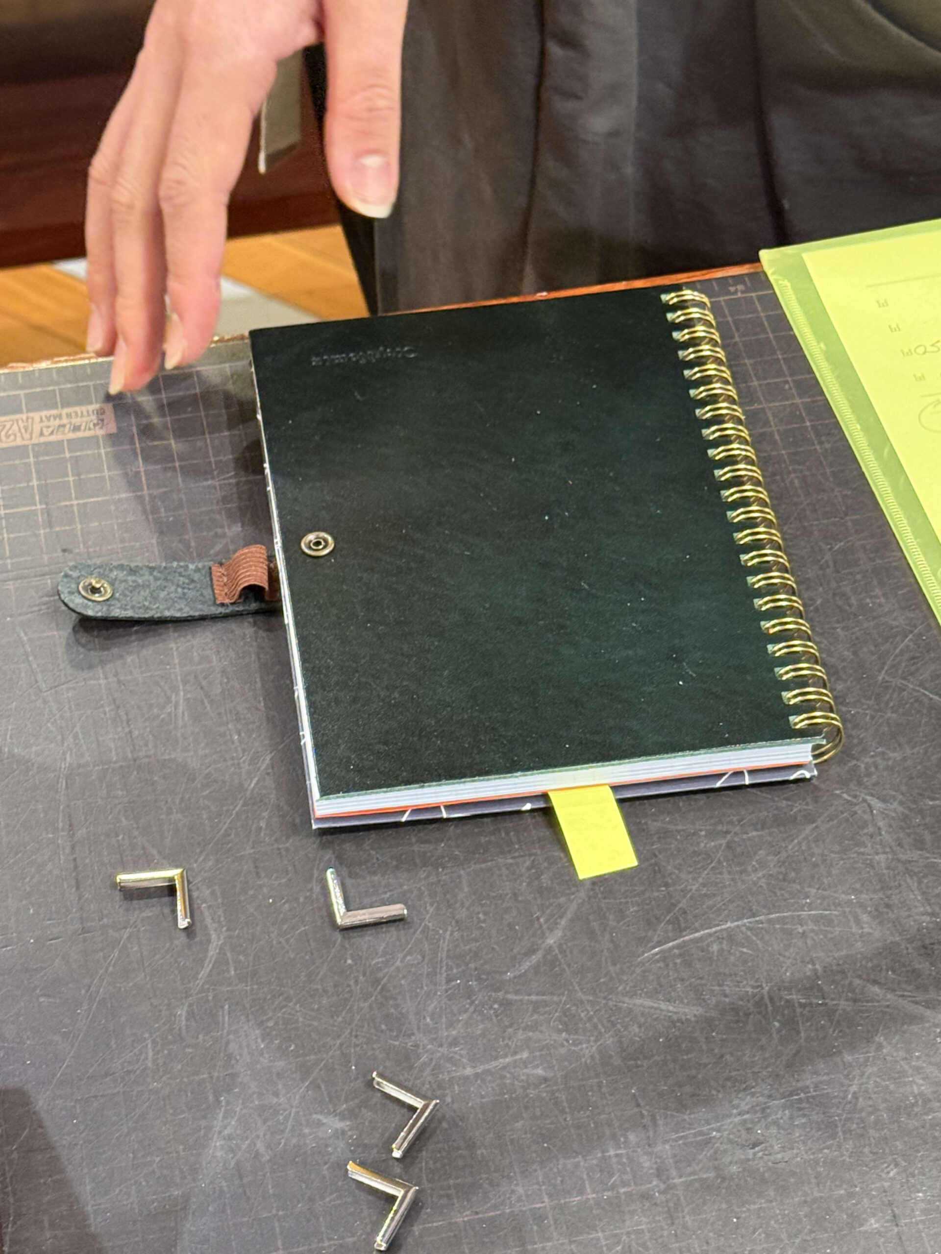 Black notebook and corner hardware on a cutting mat.