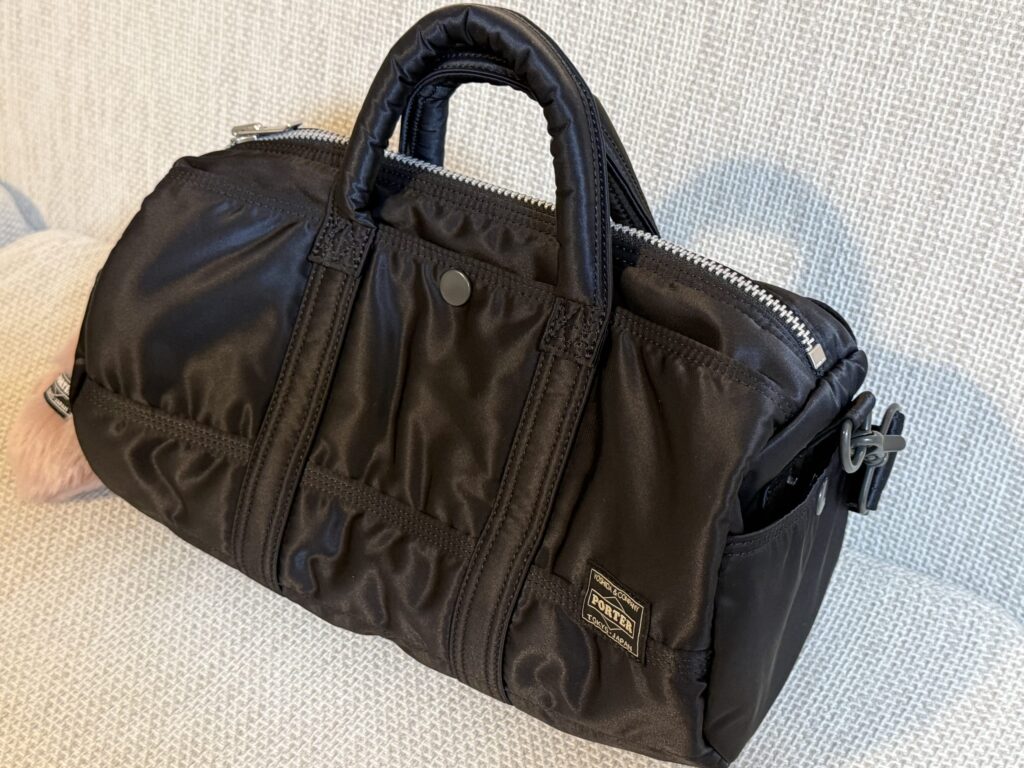 High-angle shot of a black Porter Tanker Boston bag, showing the thick aluminum zipper, side pocket structure, and metal hardware details