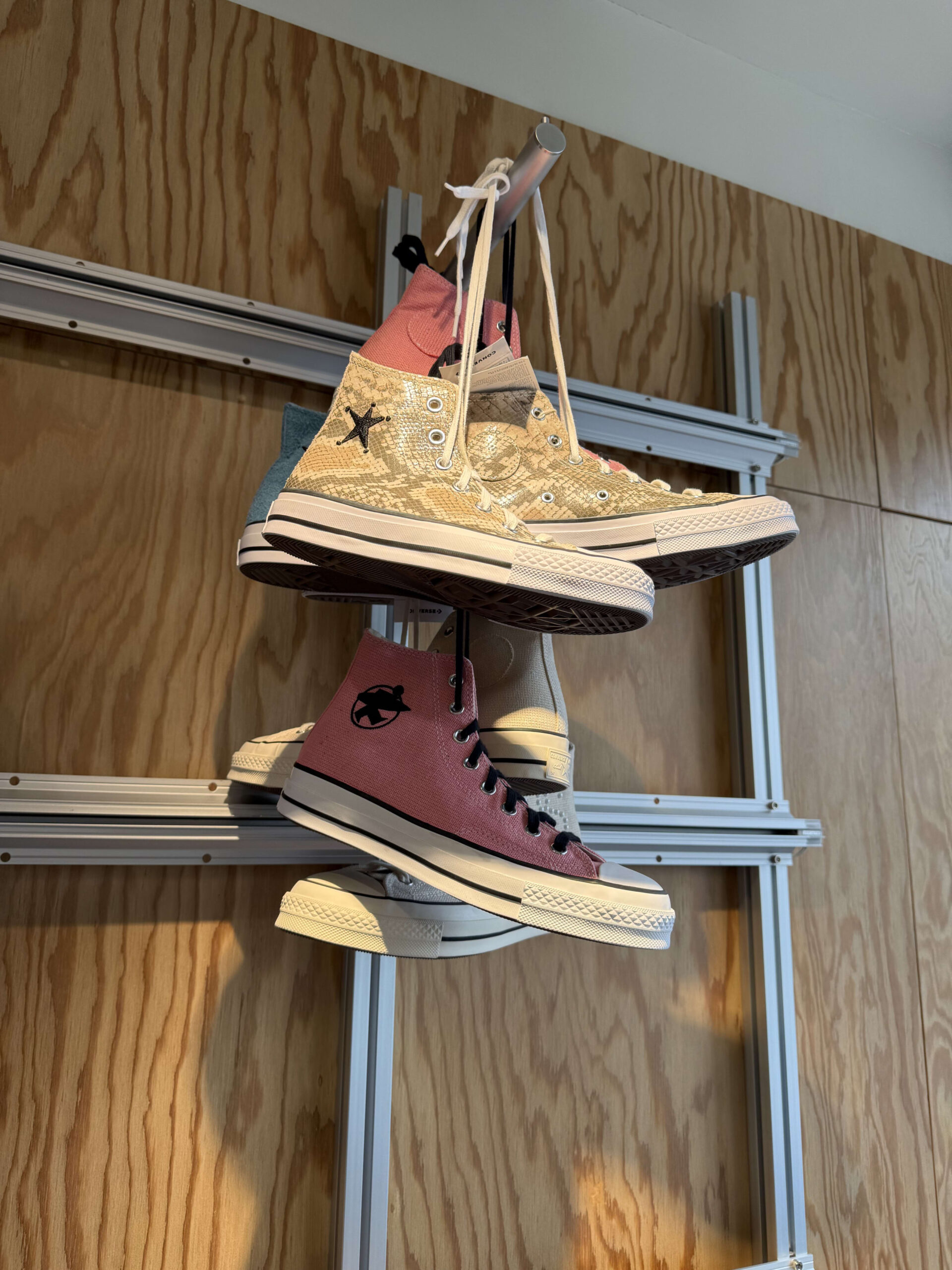 Snakeskin and pink Converse hanging by laces on a rack.