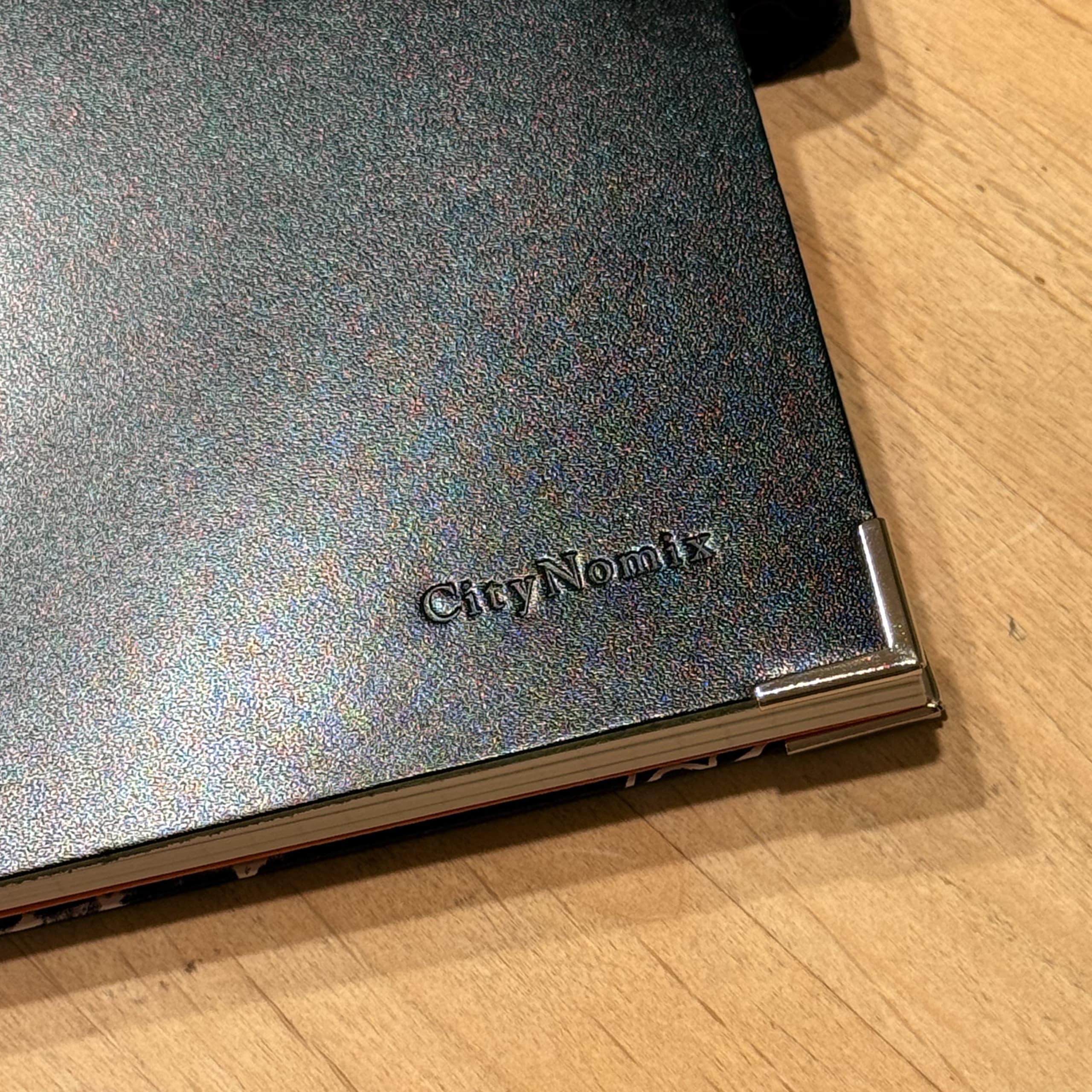 Dark notebook with CityNomix logo on a wood desk.