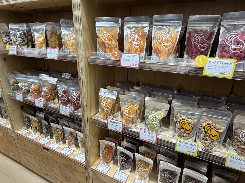 木製の棚に整然と陳列された「K nuts」ブランドの色鮮やかなドライフルーツとナッツのパッケージ