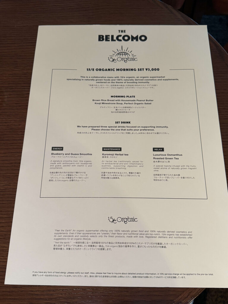 「THE BELCOMO」とオーガニックスーパー「15/E organic」がコラボレーションしたモーニングセットのメニュー表。ダークブラウンの木目調テーブルの上に置かれている。