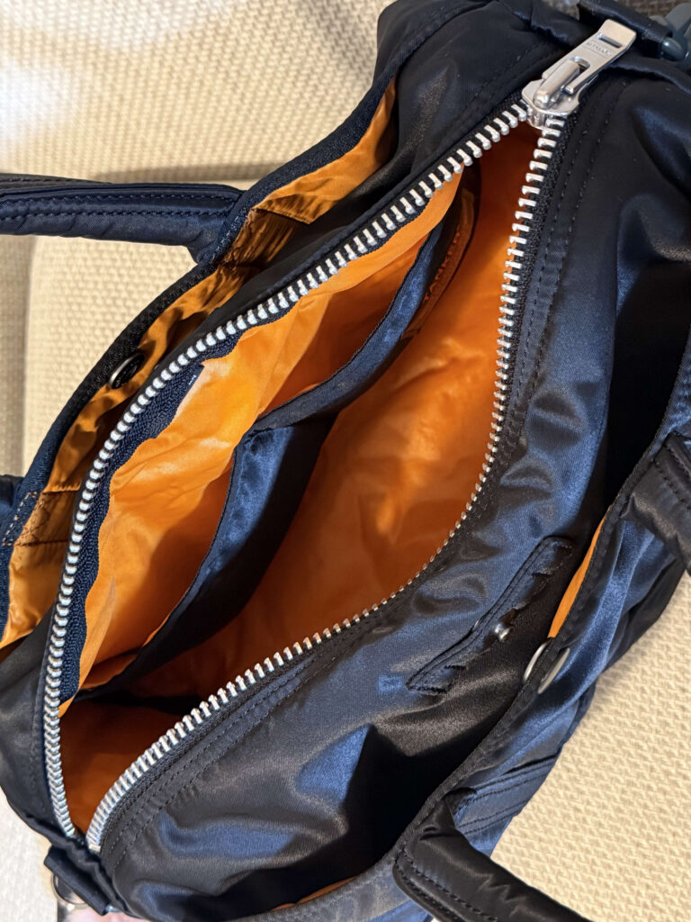 Open main compartment of a black Porter Tanker bag showing the bright rescue orange lining and internal pockets.