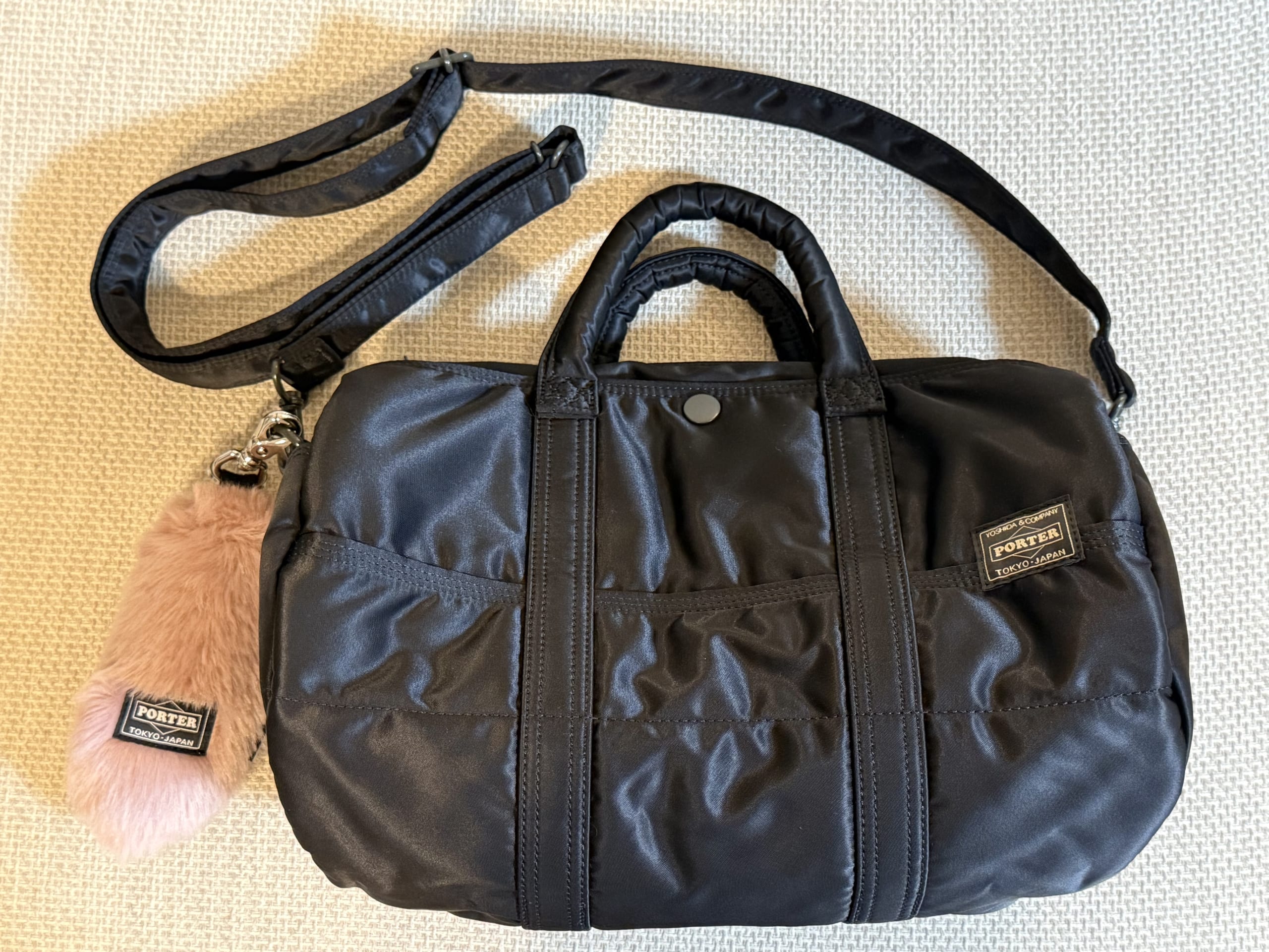 Front view of a black Porter Tanker 2WAY Duffle Bag (S) with a shoulder strap and a pink fur charm attached