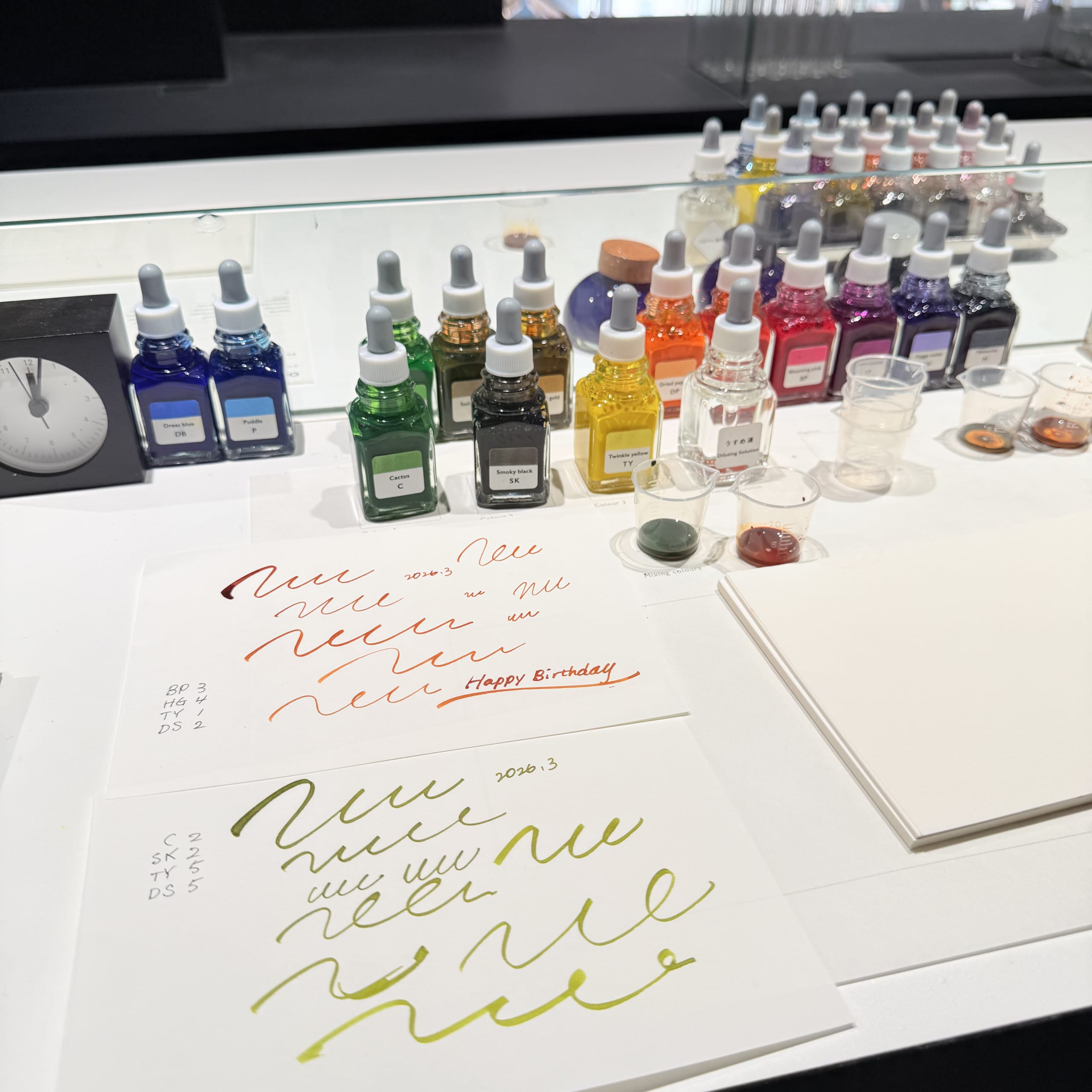 A table with ink bottles, beakers, and paper with test writing.
