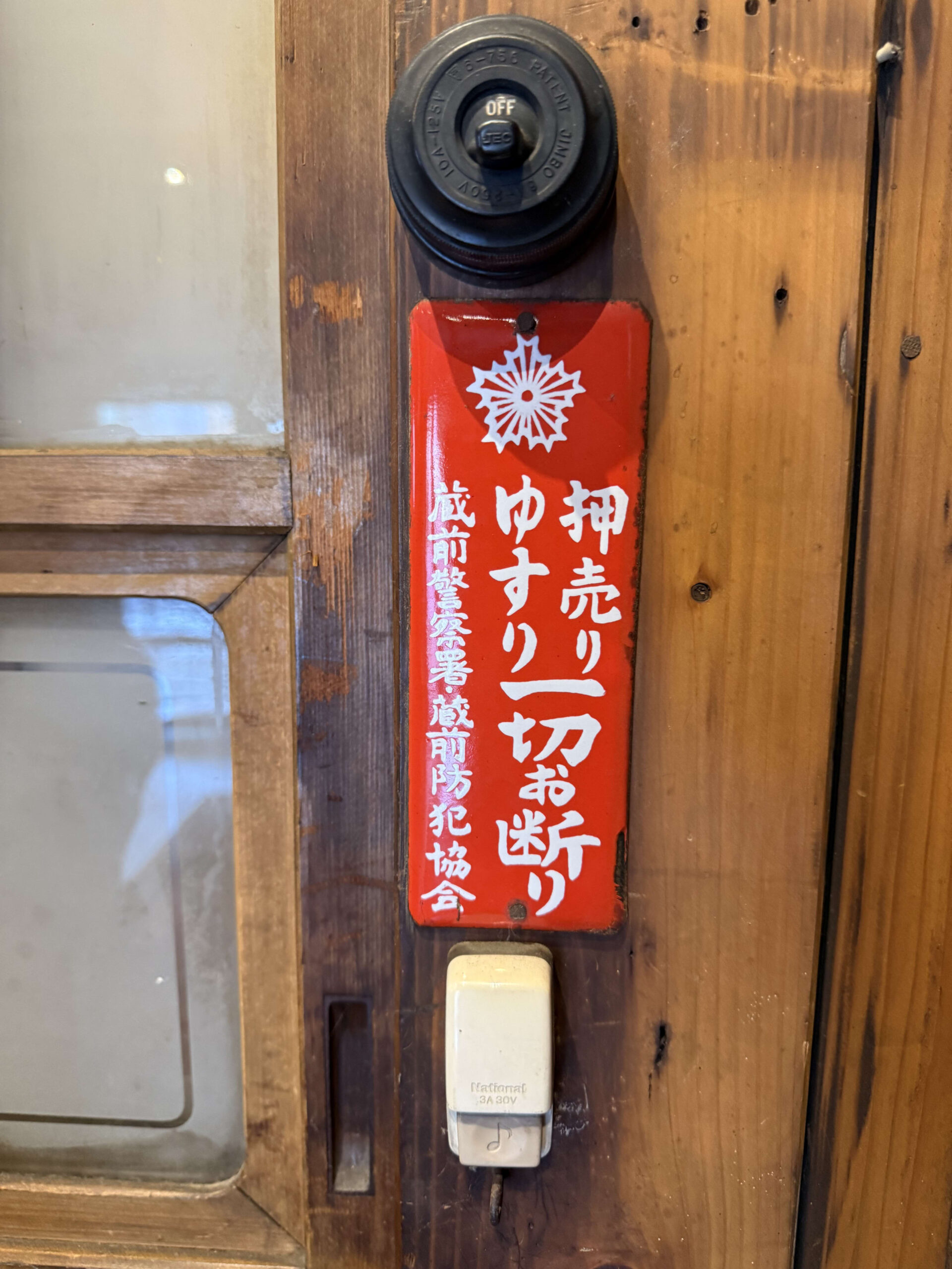 「押売りゆすり一切お断り」と書かれた赤いホーロー看板と古いチャイム。