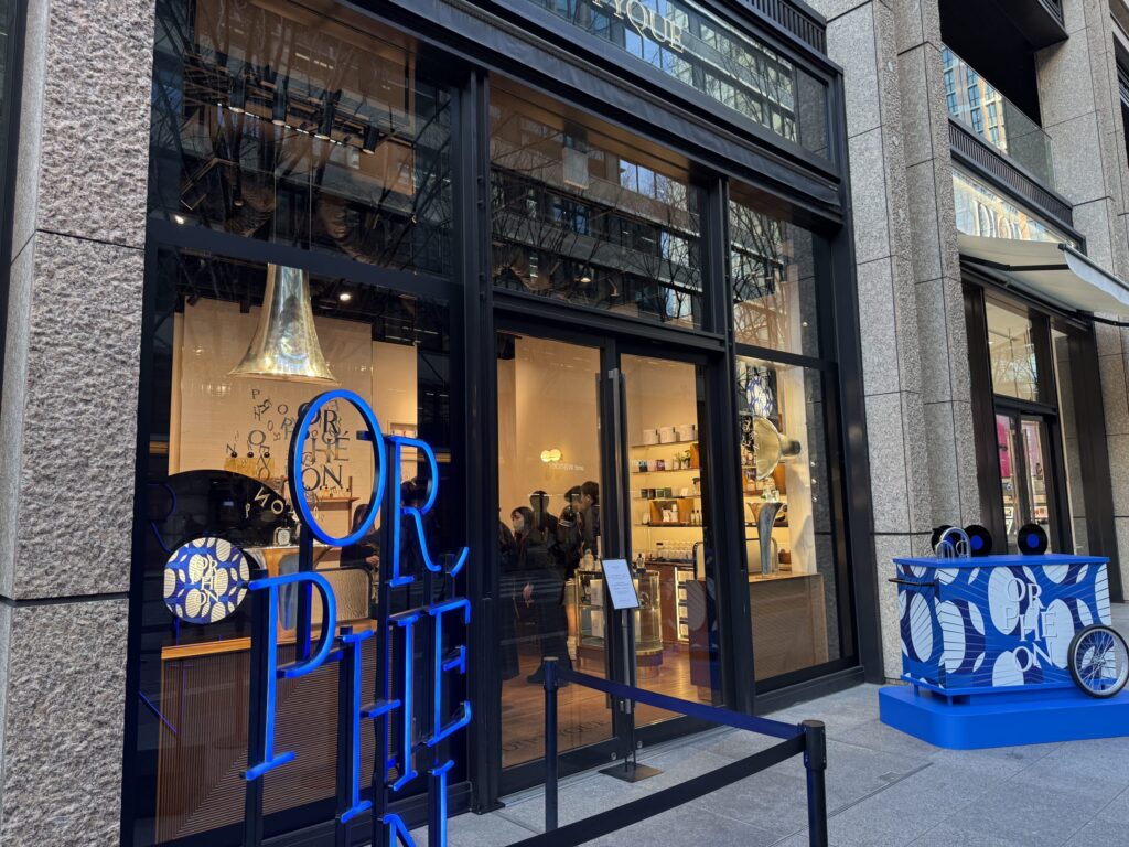 Storefront featuring a bright blue 'ORPHÉON' neon sign on the window contrasting with warm interior lighting, accompanied by a blue promotional cart outside.