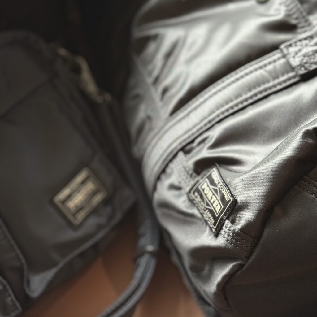 Close-up of Porter Tanker 2WAY Duffle Bag in black and Shoulder Bag in navy showing the nylon twill texture and logo