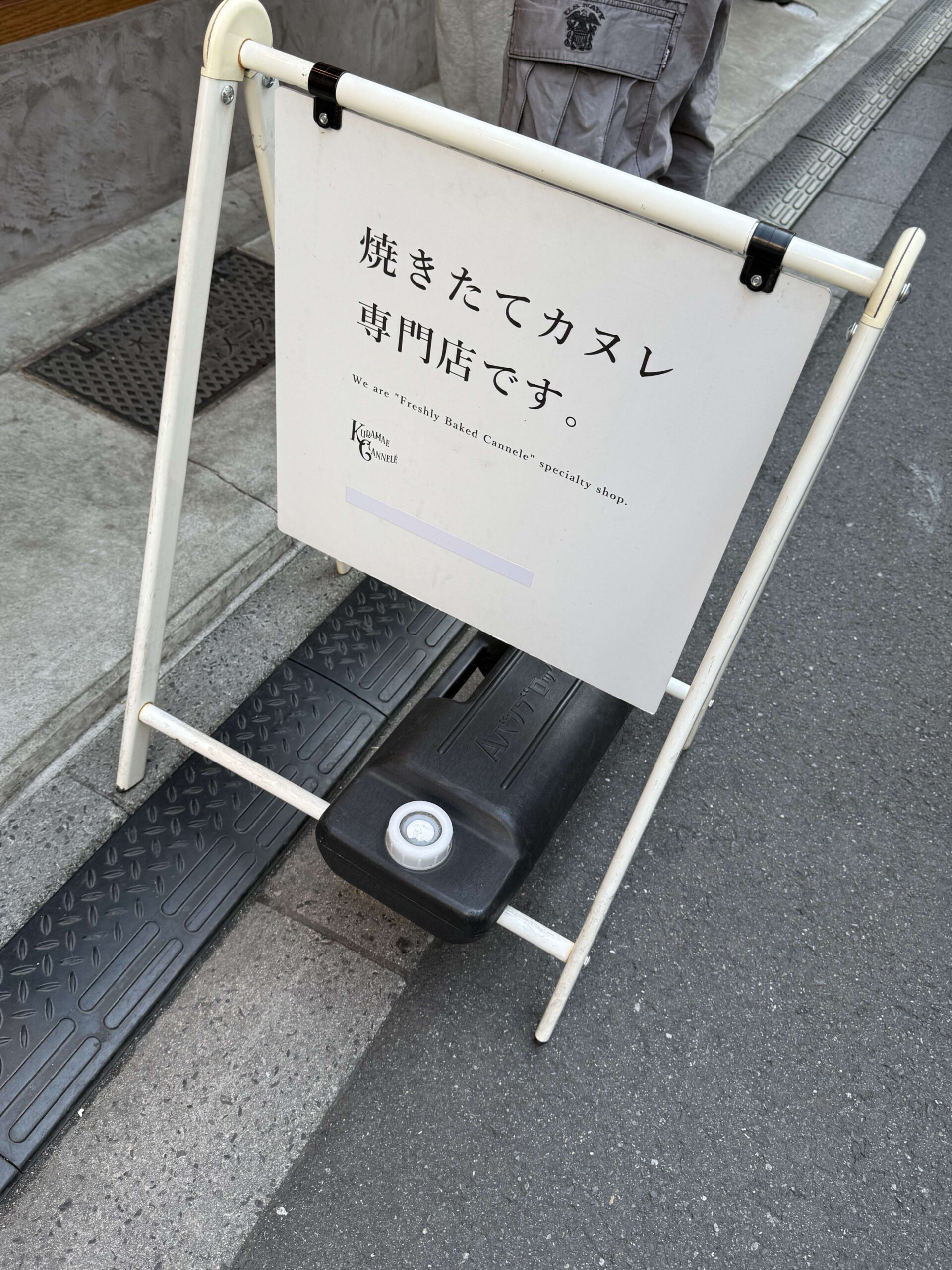 A white street sign reading 'Freshly Baked Cannele'.