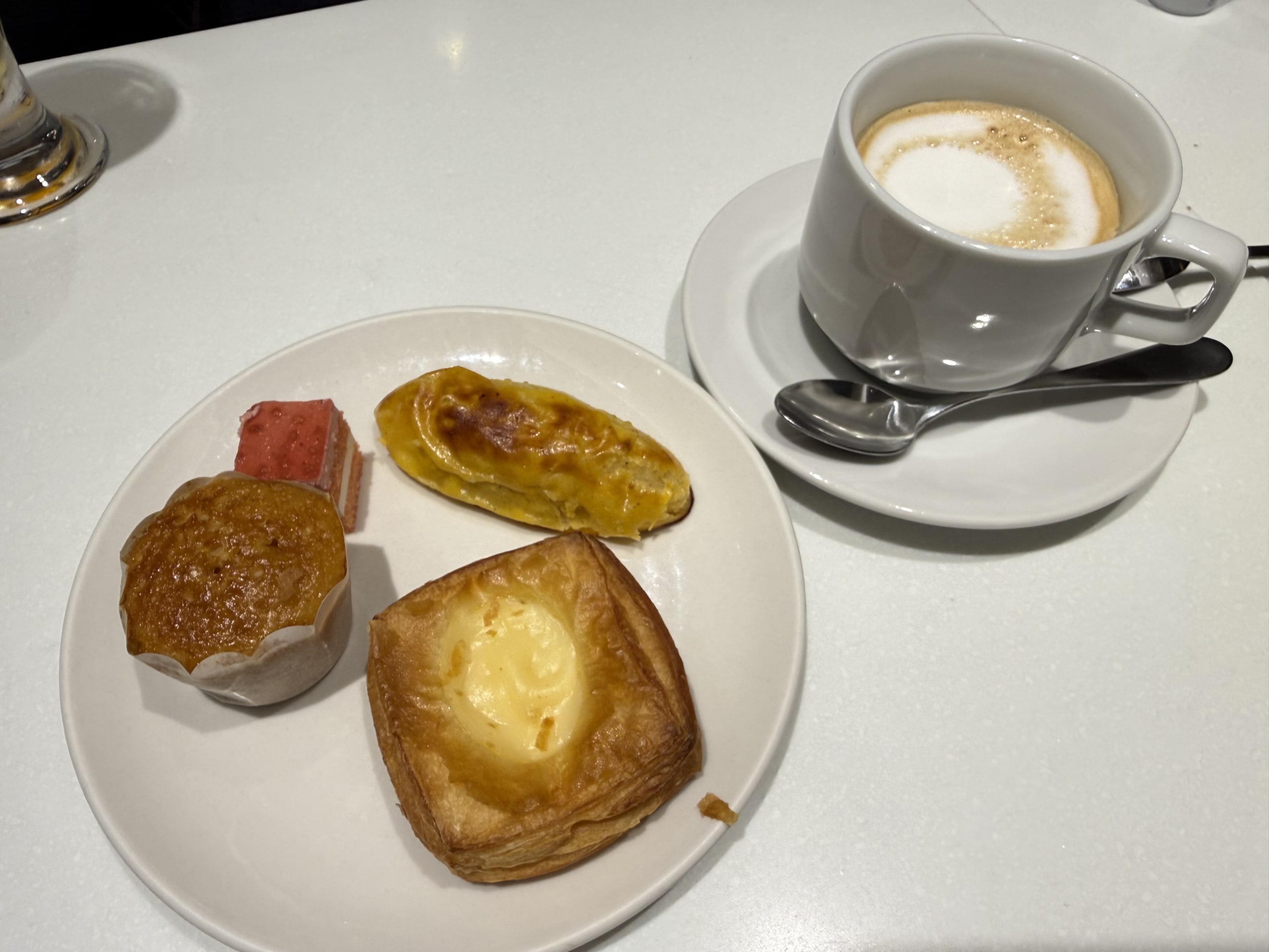 4 pastries and a cappuccino on a white table.