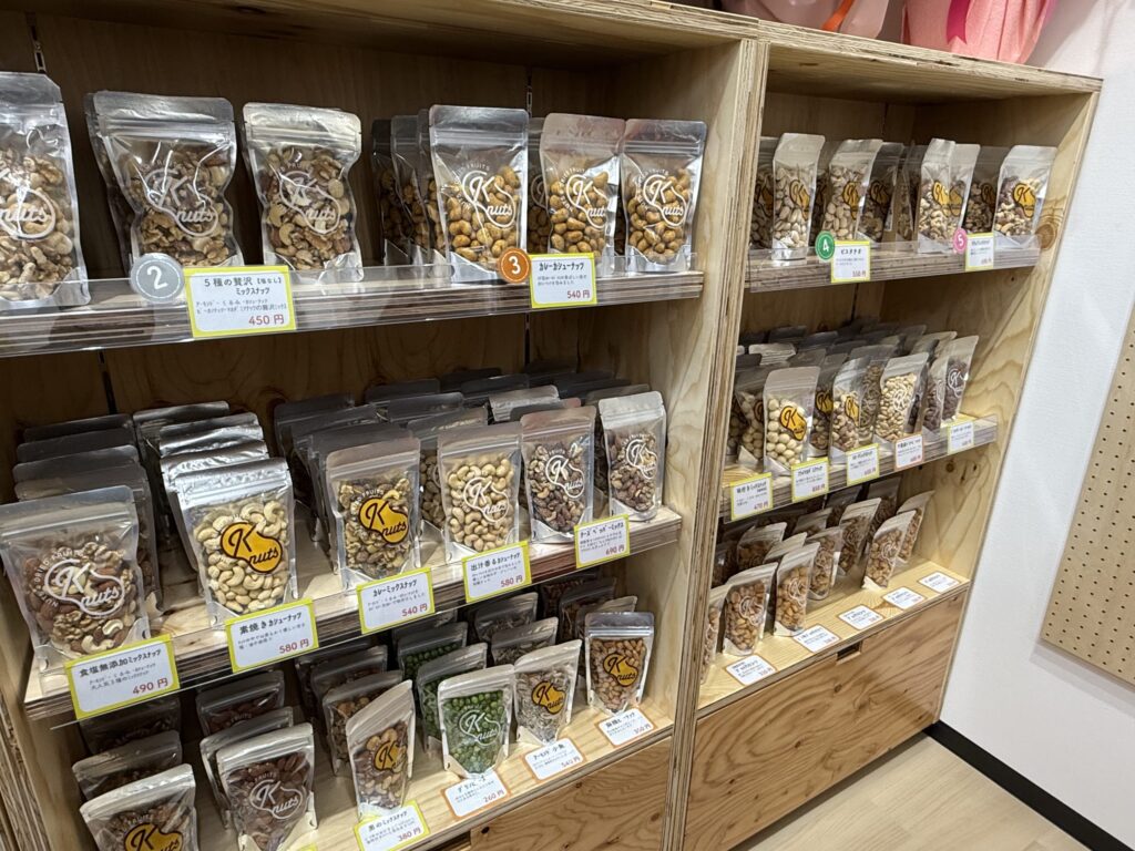 木製の棚に整然と陳列された「K nuts」ブランドの多様なナッツ商品のパッケージ