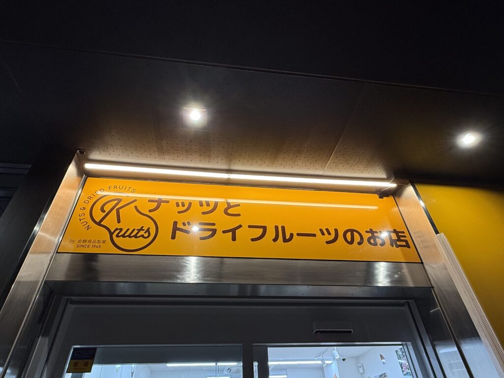 Bright yellow illuminated storefront sign for 'K nuts', a nuts and dried fruits specialty shop by Kanazuru Food Confectionery