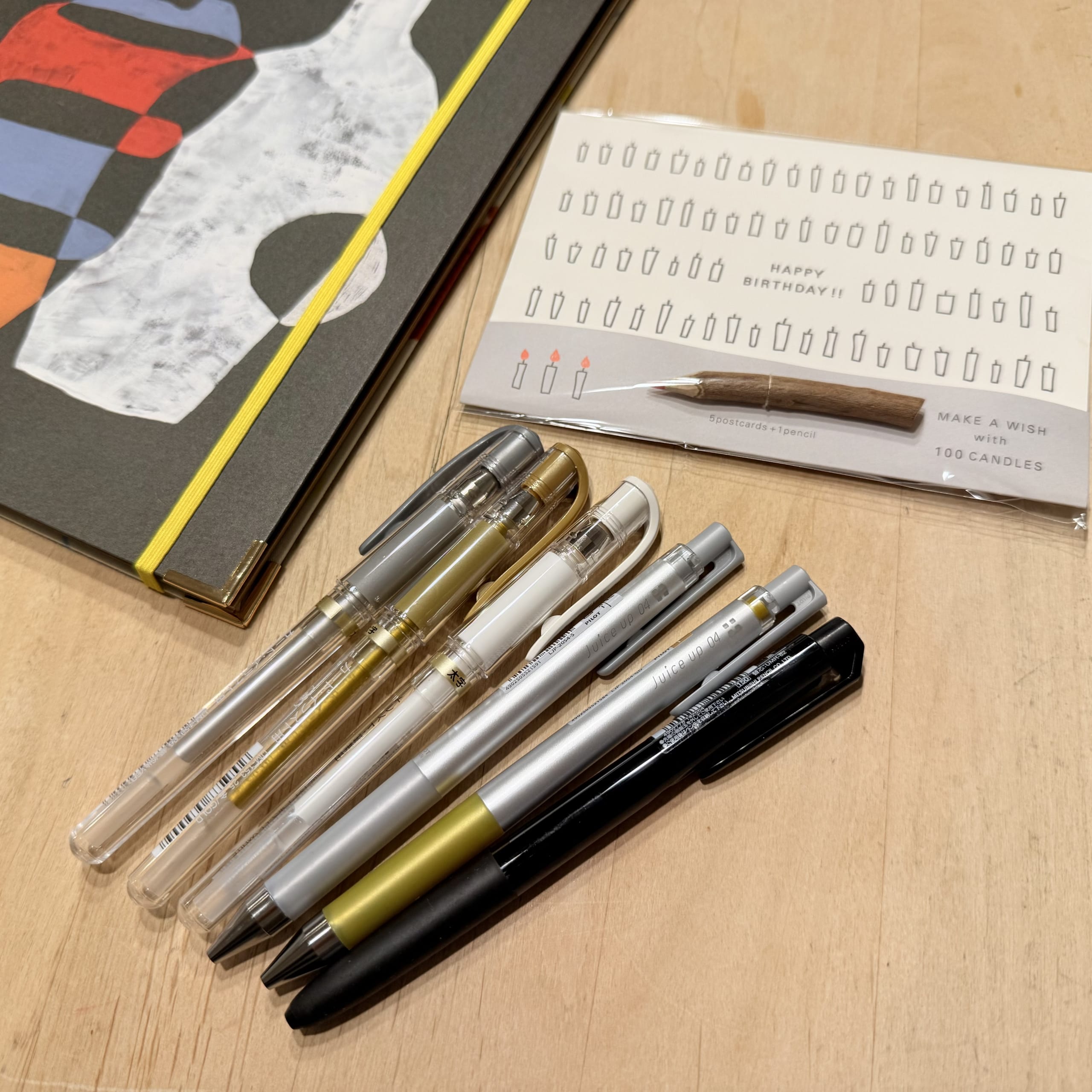 Metallic pens, a notebook and a card on a desk.